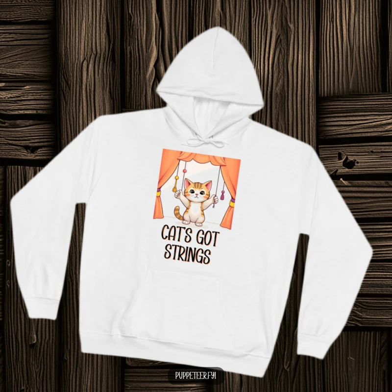 Funny curious cat batting playfully at dangling puppet strings in a colorful theater, cozy hoodie design, depicting feline curiosity in action.